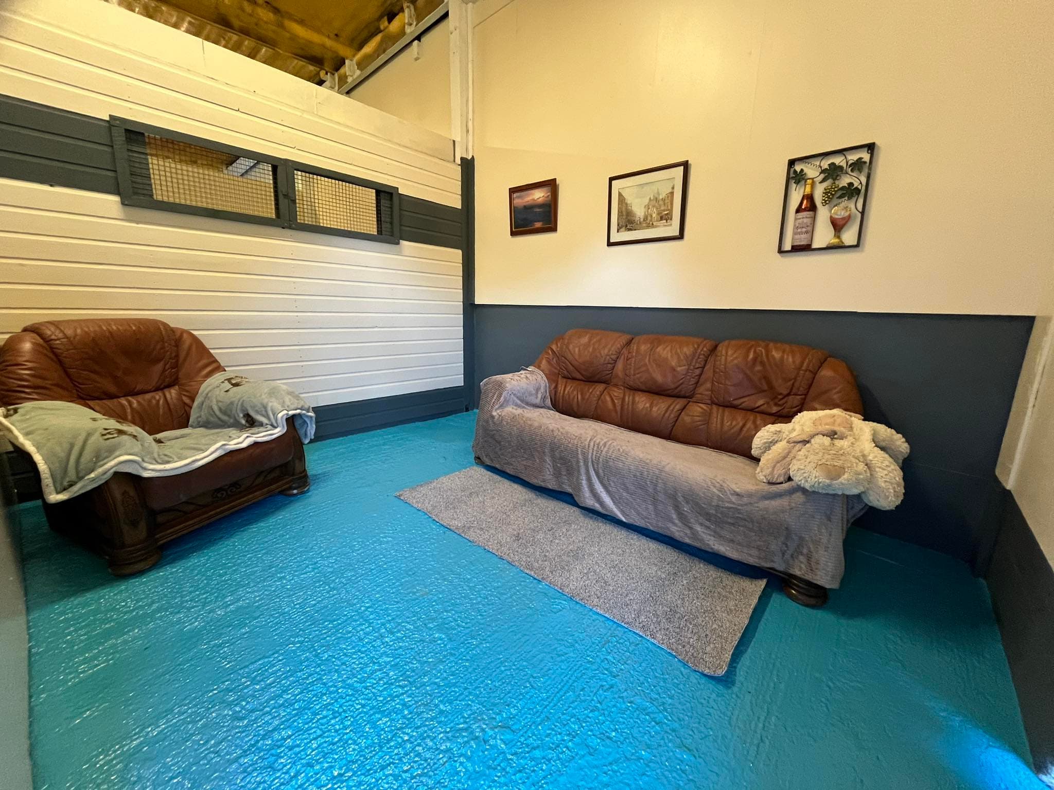 Tresmeer sofa room with two leather sofas, painted blue concrete floor and a large teddy bear